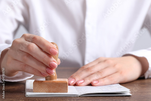 Ukraine, Lviv - September 6, 2022: Woman stamping visa page in passport at wooden table, closeup