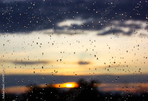 Rain at sunset. Wet window glass with raindrops against sun setting down. Autumn photo