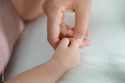 Baby holding motherʼs hand on bed, closeup
