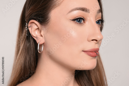 Young woman with lip and ear piercings on white background, closeup photo