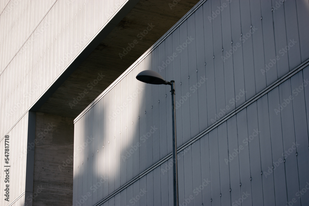 Metal street lamp against a gray blue wall in an urban urban space. Street lighting in the daytime. Monochrome photograph of elements of architecture in the style of brutalism, minimalism modern.