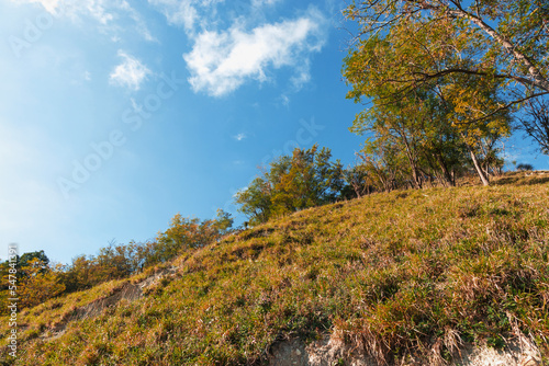 Mountain landscape with autumn forest in yellow-red foliage. A path on the mountainside on an autumn sunny day. Autumn forest under a cloudy blue sky.