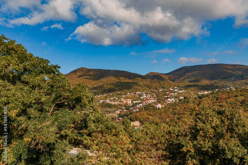 Autumn landscape in warm colors under a blue sky. A mountain landscape with a bright autumn forest under a blue sky. The mountains are covered with colorful autumn trees.