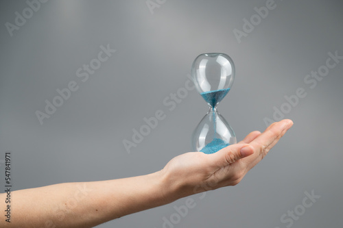 Woman holding an hourglass on a gray background. Close-up. Copy space.  photo