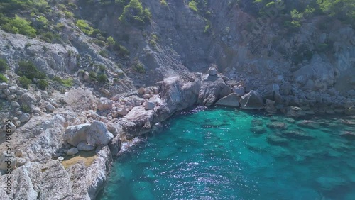 Blue lagoon surrounded by rocks and cliffs. Great aerial view flight pull back droneof ibiza Aubarca bay mountain hike cliff edge at daytime summer 2022. 4k Cinematic photo