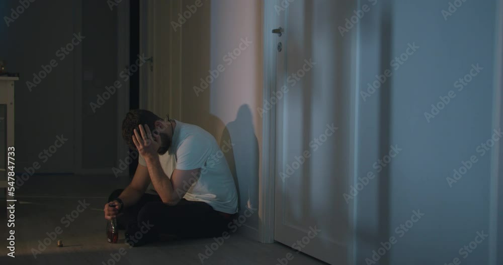 Sad Drunk Adult male sits on home floor drinking alcohol Alone at night 4k