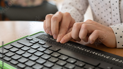 A blind woman uses a computer with a Braille display and a computer keyboard. Inclusive device. photo