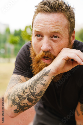 Ginger bearded sportsman resting while working out in park