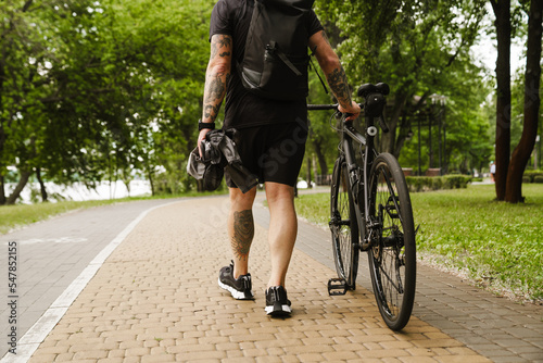 Cropped portrait from back of tattooed man walking with bicycle