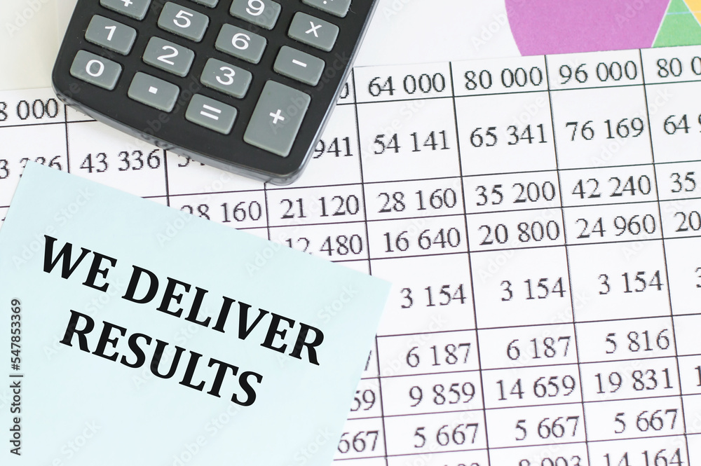 WE DELIVER RESULTS text on the white paper on light background with charts paper ,keyboard and calculator WE DELIVER RESULTS text on the white paper on light background with charts paper ,keyboard and calculator