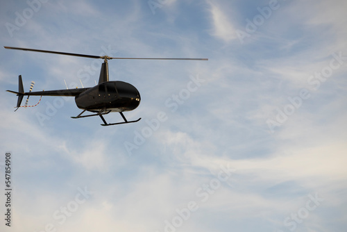 Black helicopter in air over blu sky and white clouds
