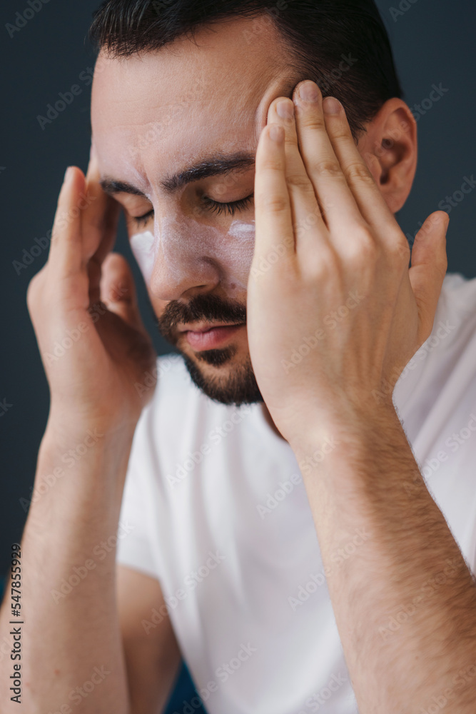Close-up portrait of a young bearded man applying face cream in bathroom. Facial treatment, cosmetology, beauty concept. Facial skincare. Concept cosmetic Close-up portrait of a young bearded man applying face cream in bathroom. Facial treatment, cosmetology, beauty concept. Facial skincare. Concept cosmetic