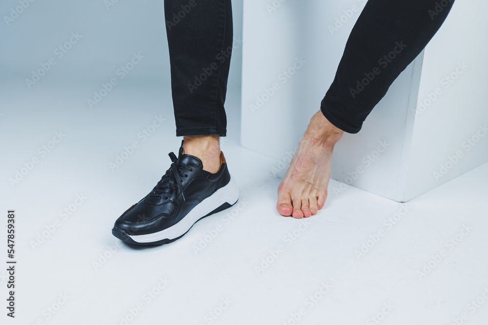 Men's feet, one in sneakers and one barefoot. Men's casual shoes. Men's feet, one in sneakers and one barefoot. Men's casual shoes.