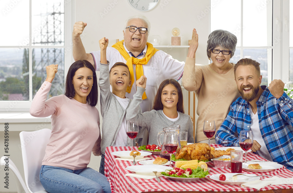 Fototapeta premium Yeah we finally gathered together. Happy cheerful mom, dad, grandma, grandpa and kids celebrating family event at home, sitting at table with chicken or turkey, enjoying festive dinner and having fun