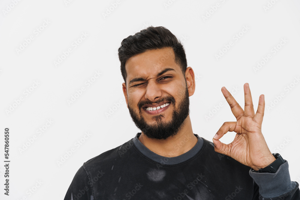 Young indian man with beard winking and showing ok sign Young indian man with beard winking and showing ok sign
