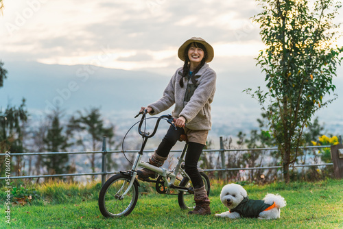 愛犬と秋冬のキャンプ場で自転車に乗ってサイクリングするアジア人女性 