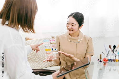 ネイルサロンでネイルチップを見ながらネイリストにカウンセリングを受ける日本人女性
 photo