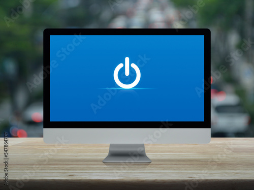 Power button icon on desktop modern computer monitor screen on wooden table over blur of rush hour with cars and road in city, Business start up online concept