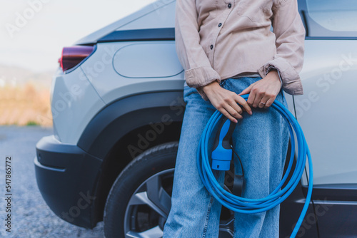 Close-up of woman holding power supply cable from her electric car, prepared for charging it in home, sustainable and economic transportation concept.