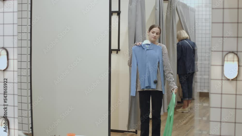 mirror reflection young female choosing clothes blue or green shirt fitting room. woman standing in front of mirror fit clothes in clothing store shop. try on new shirt coat mirror reflection young female choosing clothes blue or green shirt fitting room. woman standing in front of mirror fit clothes in clothing store shop. try on new shirt coat