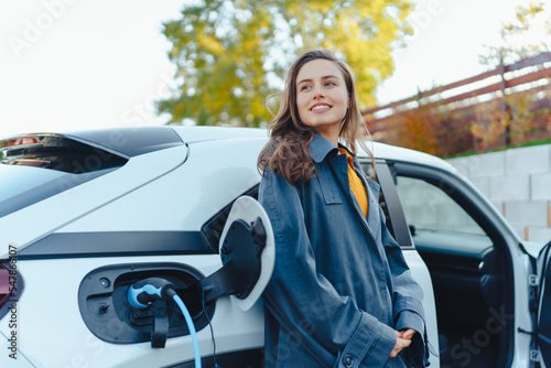 Young woman waiting while her electric car charging in home charging station, sustainable and economic transportation concept.