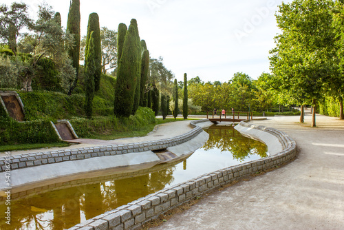 Forest of Dead - memorial monument created in memory of victims of the March 11, 2004 terrorist attacks in Madrid, Spain. Canal with water, green cypress trees, road going in distance in Retiro park.