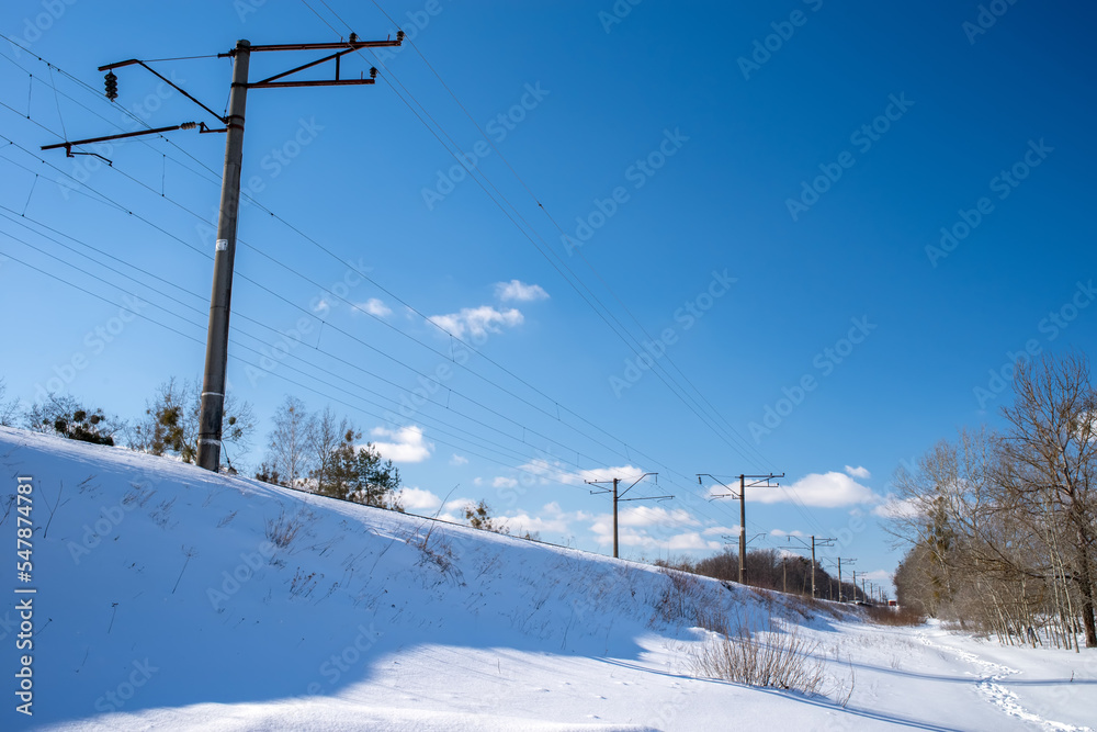 An electrified railway on an trackbed under the snow. Electric poles along the railway.