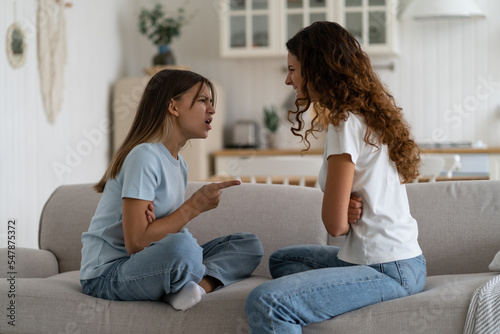 Angry emotional teen girl adolescent daughter fighting with mother parent at home while sitting in front of each other on sofa, selective focus. Problems between teenagers and parents