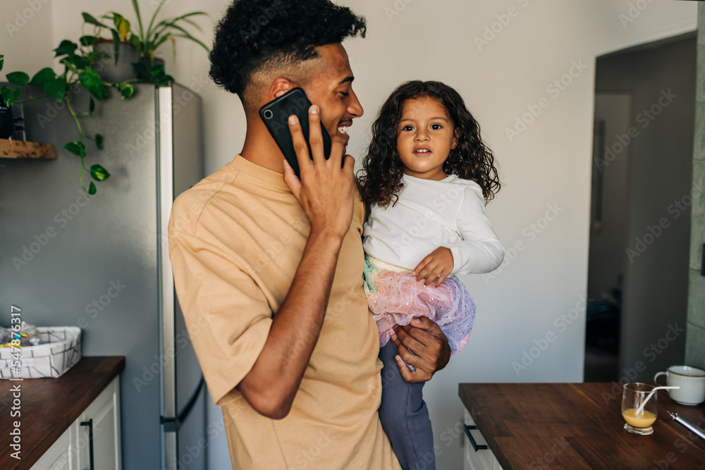 Happy young dad speaking on the phone while carrying his daughter Happy young dad speaking on the phone while carrying his daughter