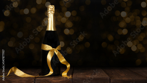 New Year Sylvester festive celebration holiday New Year's Eve greeting card background - Champagne or sparkling wine bottle with golden gift ribbon on old rustic wooden table
