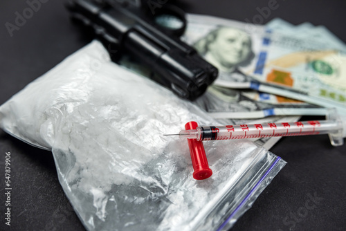 drug heroin lies next to syringes, money dollars weapons isolated on a dark background. photo