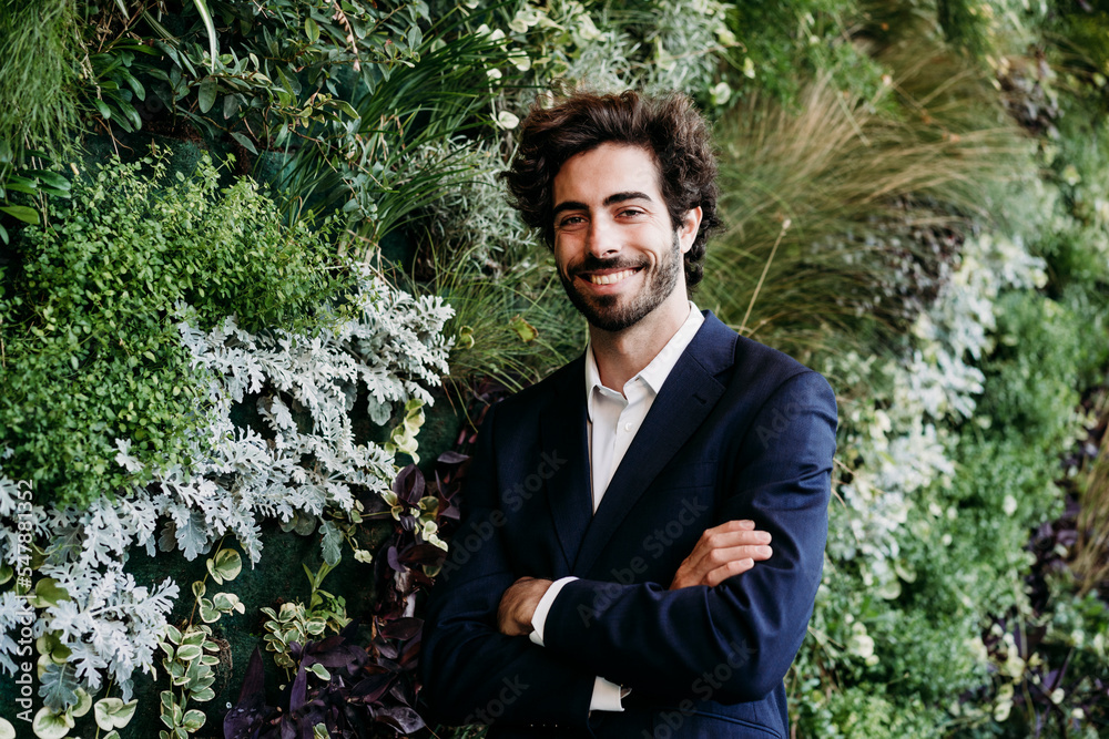 Happy businessman with arms crossed by plants Happy businessman with arms crossed by plants