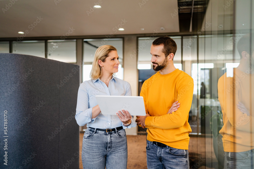 Young businessman with arms crossed looking at colleague holding tablet PC in office Young businessman with arms crossed looking at colleague holding tablet PC in office