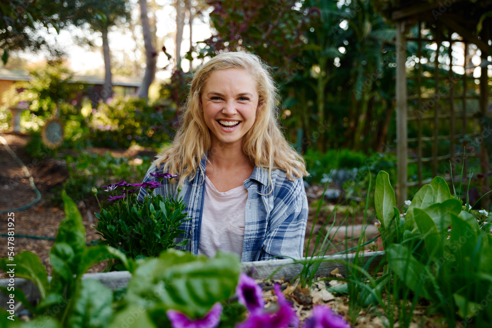 © StratfordProductions - Young caucasian woman wearing checked shirt looking at camera by flowers in plant nursery