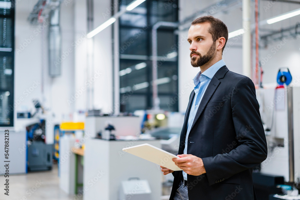 Young businessman with tablet PC standing in factory Young businessman with tablet PC standing in factory