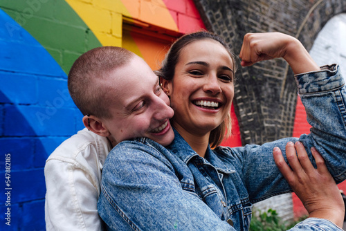 Happy lesbian woman showing biceps in front of rainbow wall photo