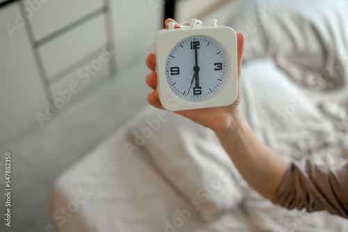 Hand of woman with alarm clock in bedroom