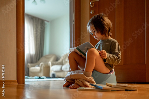 Cute boy sitting on potty and reading book at home photo