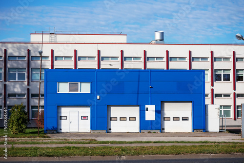 An industrial building with a blue metal building and a white building behind it on a sunny and cloudy day
