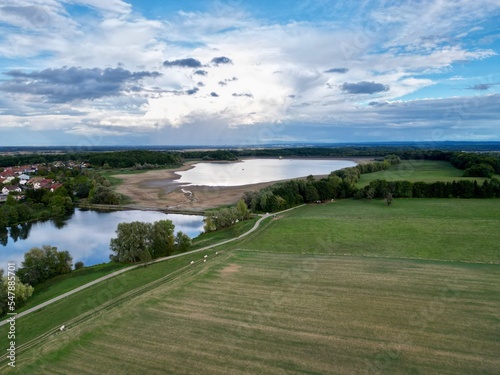 Panoramic aerial drone top view of the Michelbach lake dam (Upper-Rhine, Alsace, France) and its forest, village, mountains and meadow, in drought summer cloudy weather, with very low water level