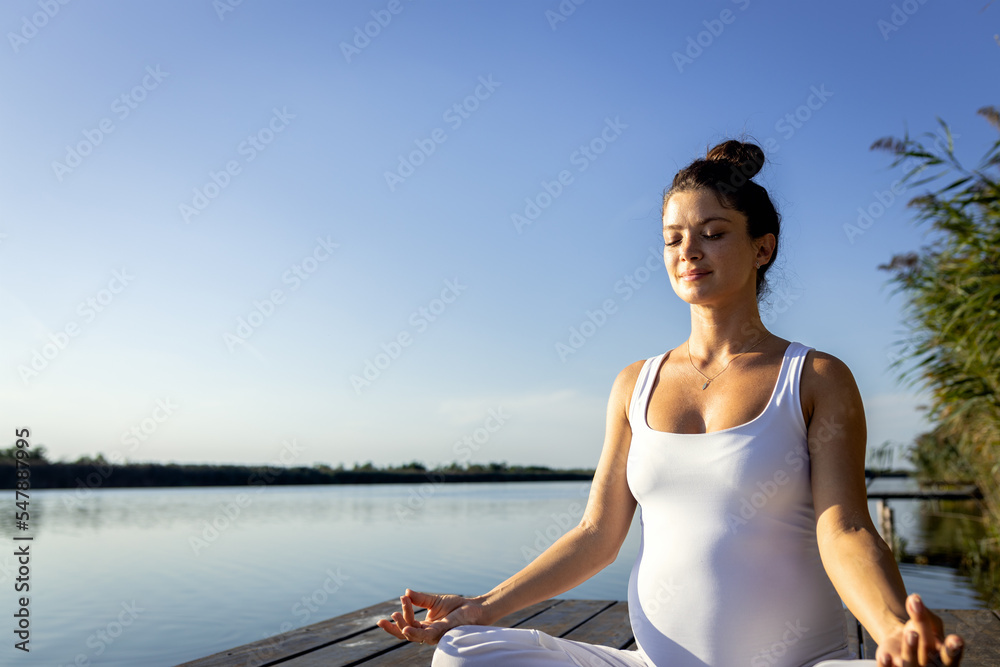 Pregnant woman doing yoga at lake during the day.