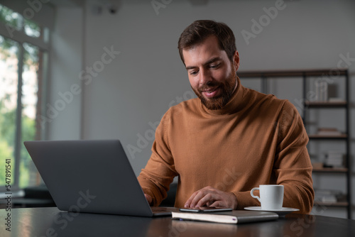 Smiling businessman in casual wear working on laptop at office