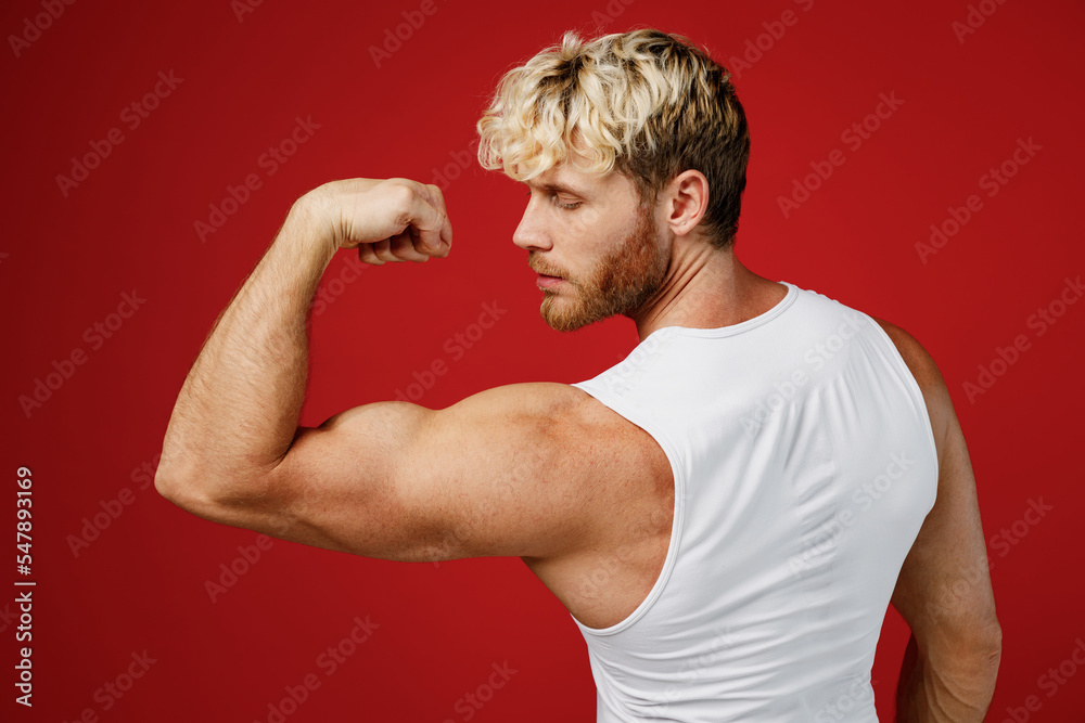 Side back view young strong sporty toned sportsman man 20s wear white clothes spend time in home gym show biceps muscle on hand power isolated on plain red background Workout sport fit body concept Side back view young strong sporty toned sportsman man 20s wear white clothes spend time in home gym show biceps muscle on hand power isolated on plain red background Workout sport fit body concept