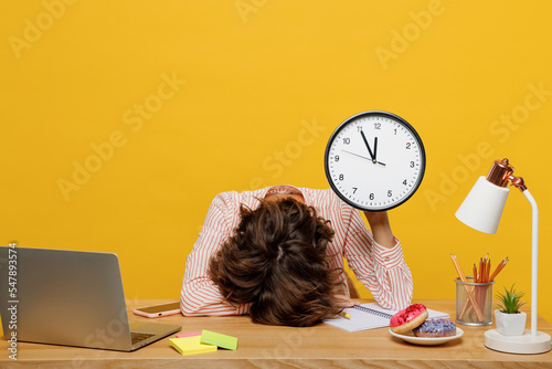 Foto Young sleepy employee business woman wear casual shirt sit work at office with pc laptop hold in hands clock put head down on desk isolated on plain yellow color background Achievement career concept