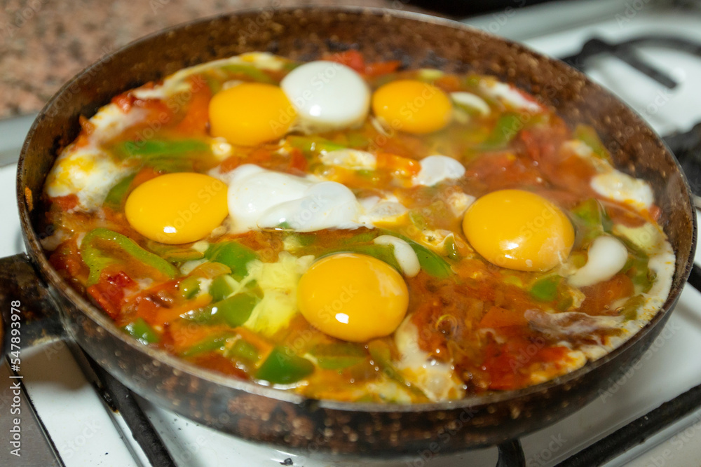 Cooking of Shakshuka, traditional dish with eggs, onion, tomatoes and peppers in the frying pan, kitchen homemade, close-up Cooking of Shakshuka, traditional dish with eggs, onion, tomatoes and peppers in the frying pan, kitchen homemade, close-up