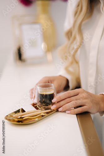 Close-up of woman take cup of coffee during waiting for cosmetology procedure. Transparent glass with a double bottom. Espresso