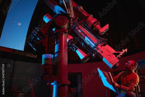 Fototapeta Astronomer with a big astronomical telescope in observatory doing science research