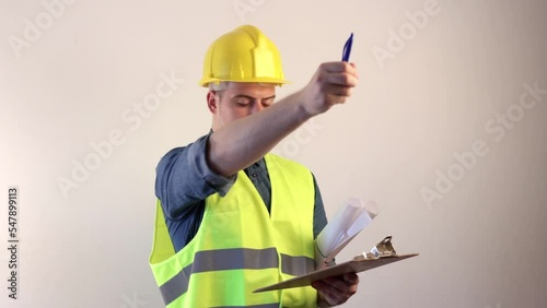 Construction architect wearing a yellow vest and hard hat is taking notes on the job site.