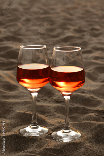 Glasses of tasty rose wine on sand