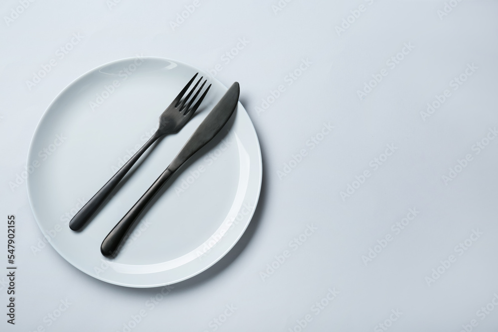 Clean white plate with cutlery on light grey background, top view. Space for text Clean white plate with cutlery on light grey background, top view. Space for text